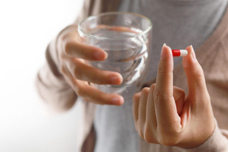 Nainen pitelee lääkekapselia ja vesilasia.