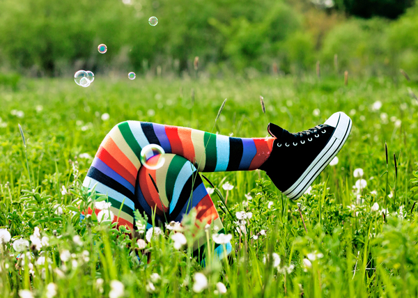 Värikkäisiin sukkahousuihin pukeutuneen henkilön jalat niityllä