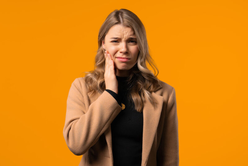 Kaunis nainen pitelee kädellä kiinni poskesta ja näyttää tuskaiselta.