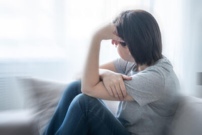 Nuori nainen istuu sohvalla ja nojaa otsaa käsiinsä.