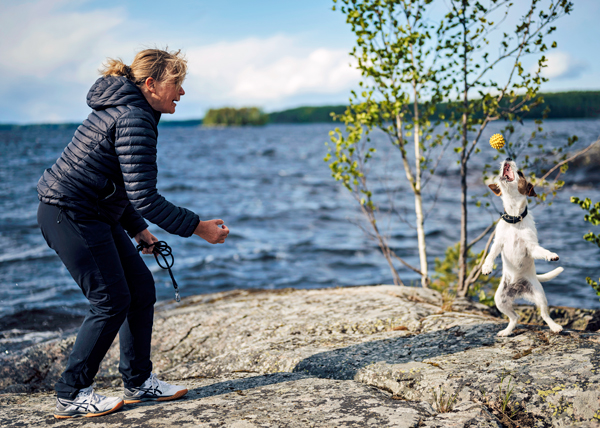 Auli Riihiaho heittää keltaista palloa Hilla-koiralle kallioisella rannalla.