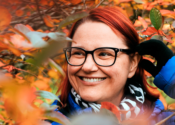 Lähikuva punahiuksisesta hymyilevästä Mia Raassinasta syksyisessä puistossa.