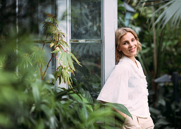 Laura Allonen nojaa pylvääseen kasvitieteellisessä puutarhassa ja katsoo hymyillen kameraan.