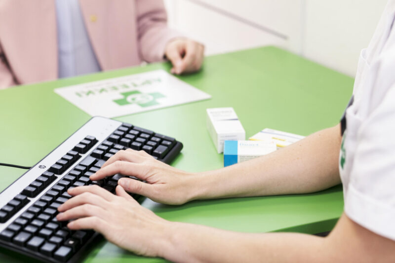 Kuva apteekin reseptitiskistä, jossa farmaseutti kirjaa tietoja koneelle.