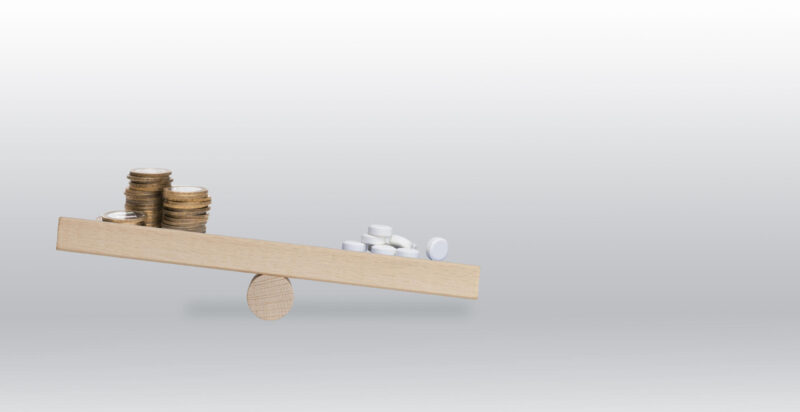 vaaka, jonka toisella puolella lääkkeet, toisella rahat