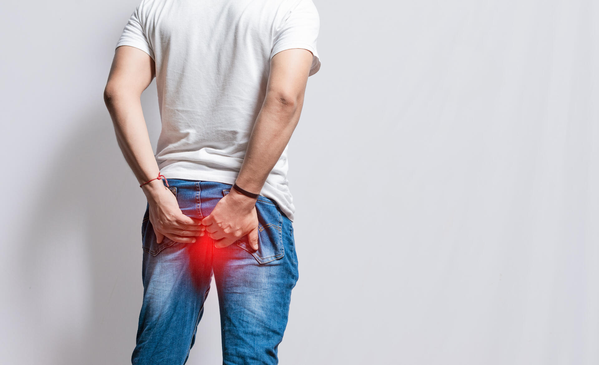 Mies takaapäin, hänellä on yllään valkoinen t-paita ja farkut. Hän pitelee käsillään kiinni takapuolesta, jonka kohdalla kuvassa on punainen tehosteväri kuvaamassa kuumotusta.