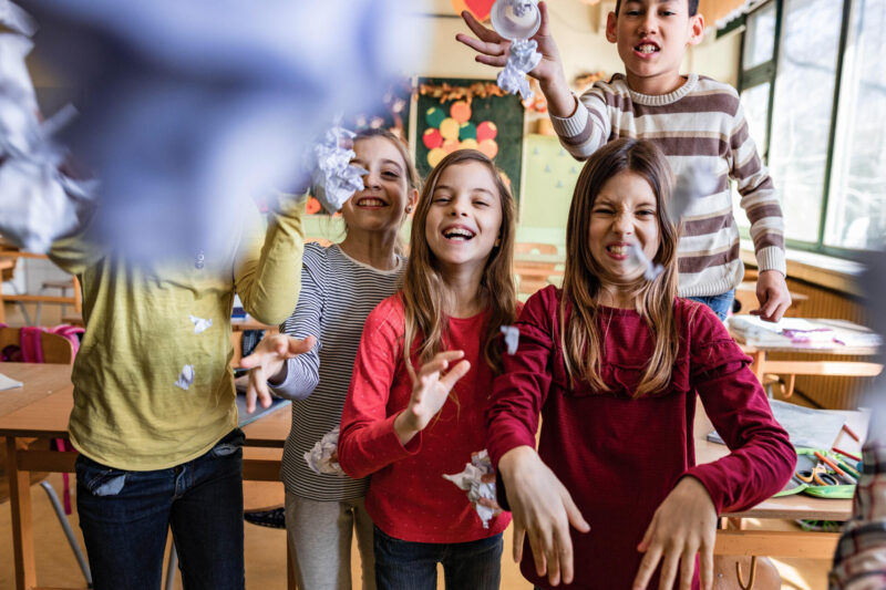 Joukko iloisia lapsia luokkahuoneessa.