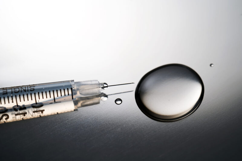 Harmaasävyinen lähikuva ruiskusta ja tipasta lääkeainetta.