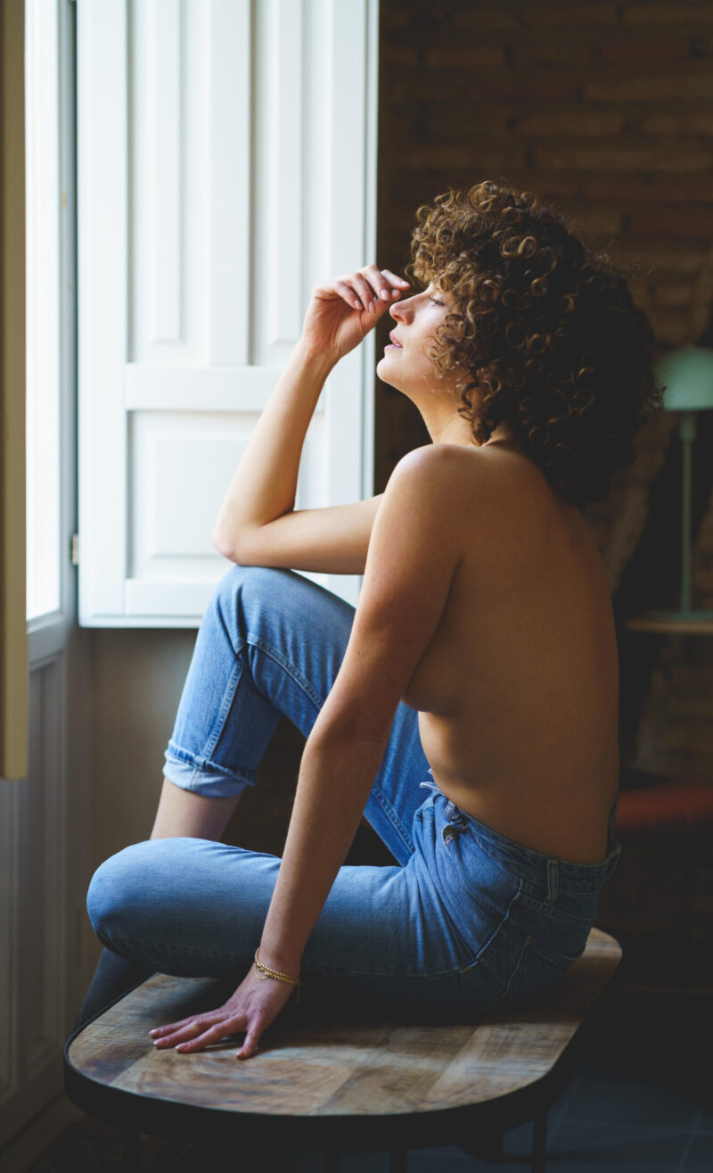 Nuori nainen istuu penkillä avoimen ikkunan edessä ja rentoutuu silmät suljettuna.