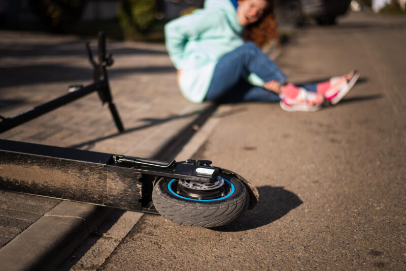 Tyttö on kaatunut sähköpotkulaudalla ja pitelee selkäänsä.