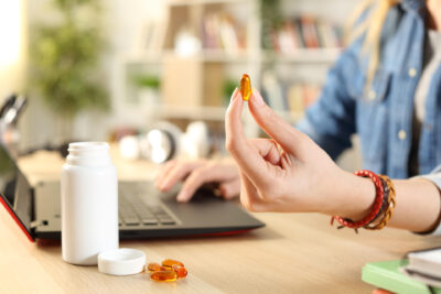 Nuori nainen pitää kädessään kapselia ja katsoo samalla tietokonetta.