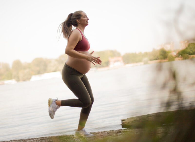 Raskaana oleva nainen lenkkeilee veden äärellä.