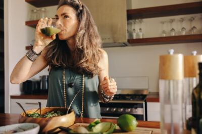 Keski-ikäinen nainen nauttii terveellistä kasvissmoothieta keittiössä.
